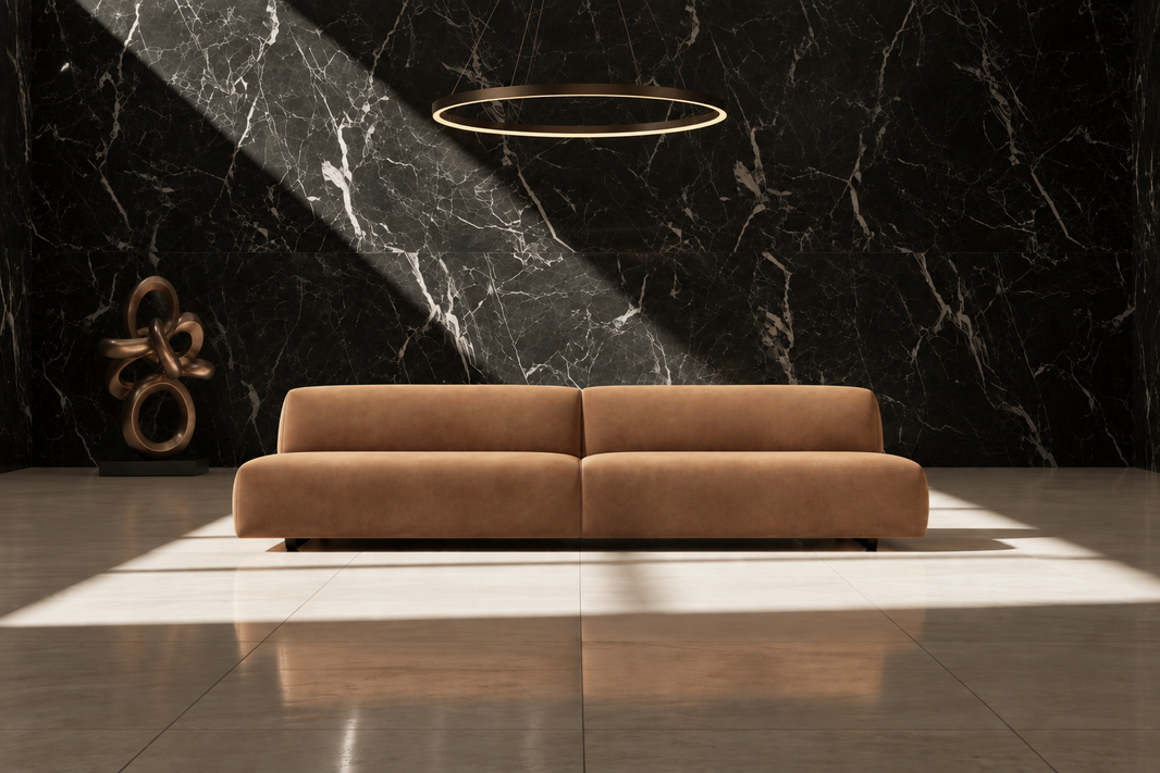 A modern tan leather sofa centered against a black marble wall with dramatic diagonal sunlight and shadows. A thin circular gold pendant light hangs above, and a sculptural bronze object sits to the left.