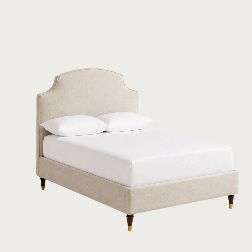 An upholstered beige bed frame with a curved headboard and matching footboard, shown with a white mattress and two white pillows.