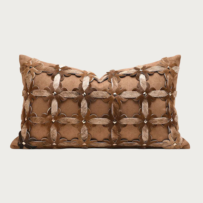 A rectangular brown decorative throw pillow with a textured, woven geometric pattern of overlapping leather-like strips and small metallic studs, shown against a plain light gray background.