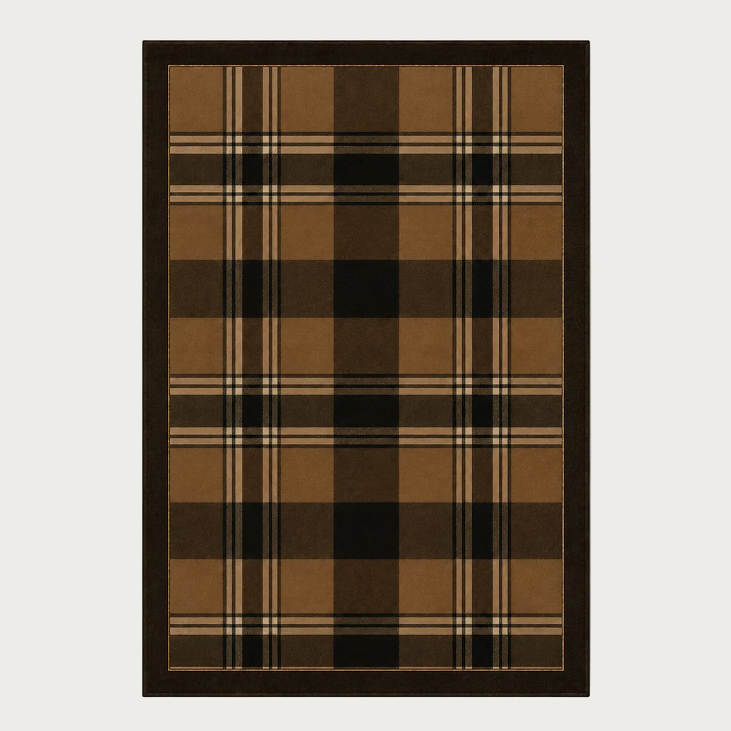 A rectangular area rug with a classic plaid pattern in shades of brown, tan, black, and beige, finished with a solid dark brown border, shown against a neutral light gray background.