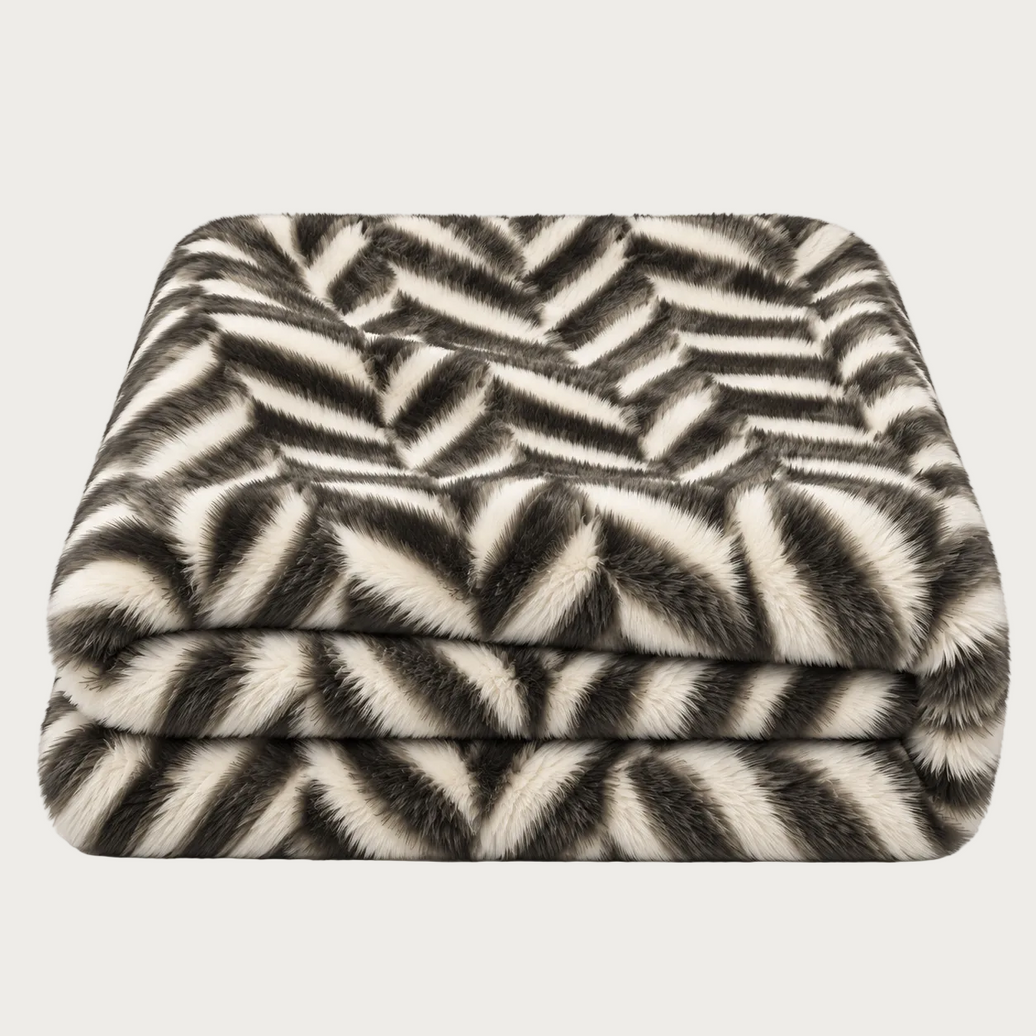 A folded throw blanket with a black and off-white chevron pattern, featuring a soft faux fur texture, shown against a plain white background.