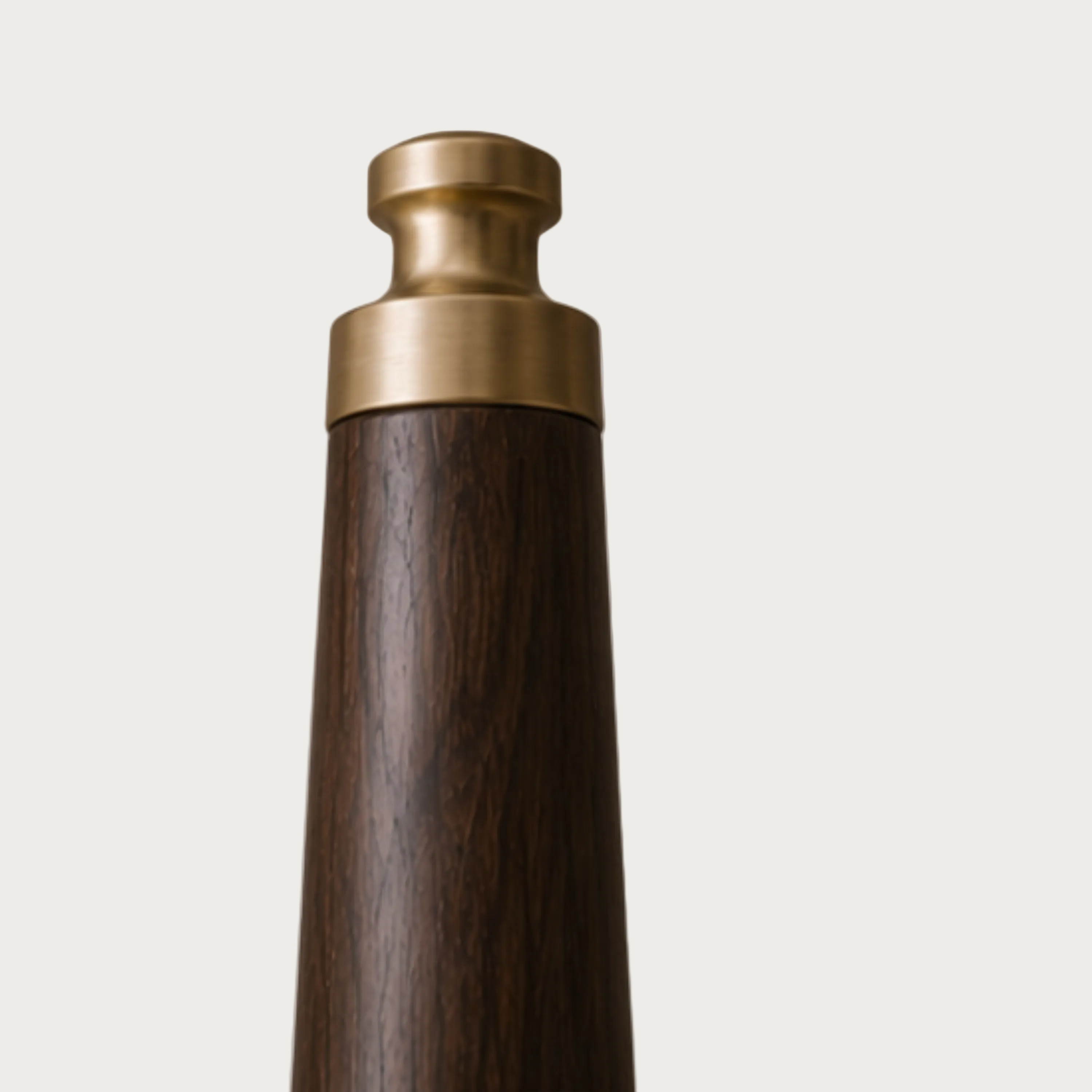 Close-up of the top portion of a dark wood and brass cylindrical object against a light gray background.