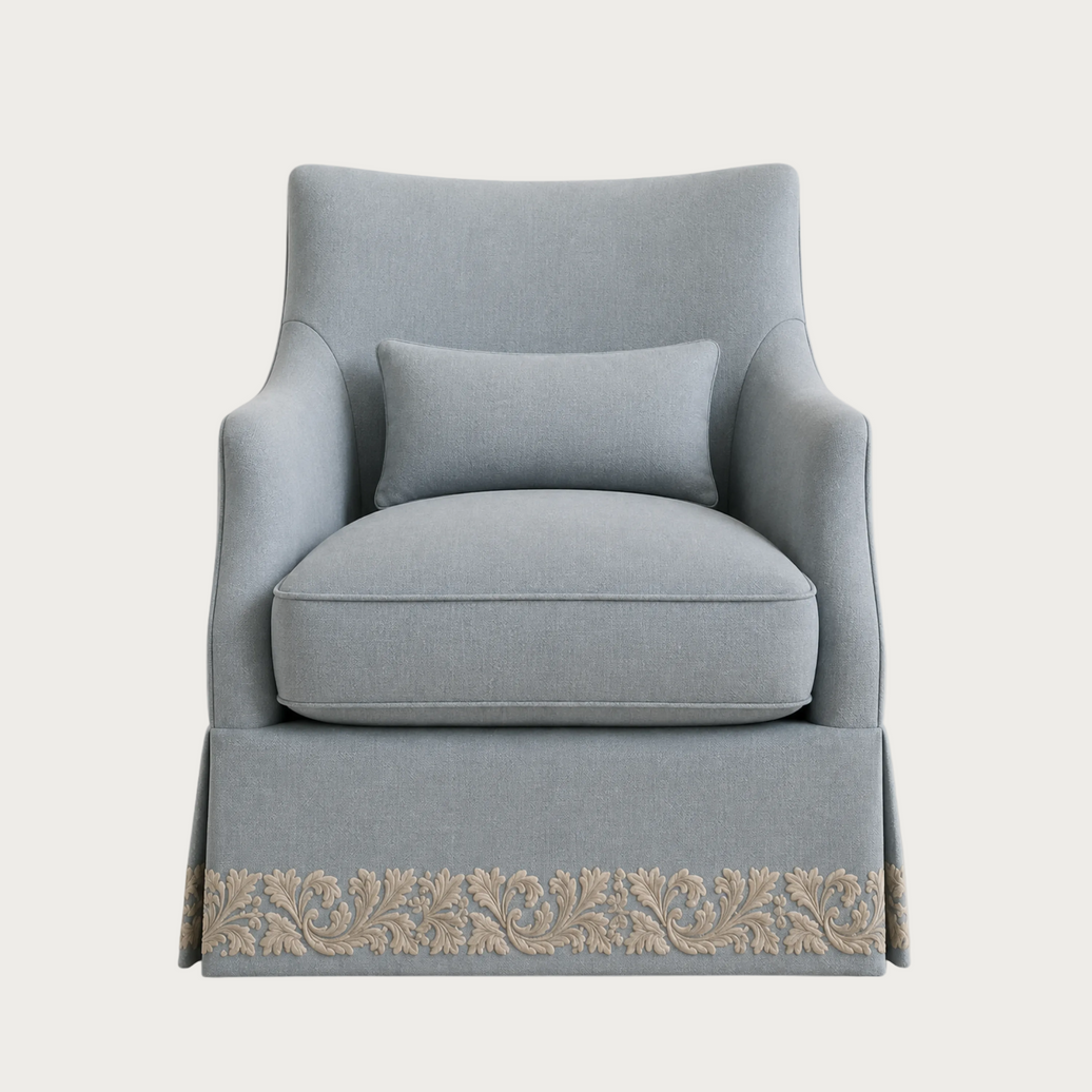 A light blue upholstered armchair with a matching lumbar pillow and a decorative beige floral border along the skirt, shown against a plain light gray background.