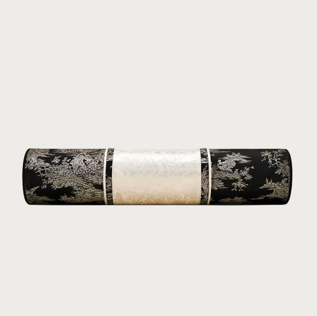 A cylindrical decorative pillow, featuring a black and silver landscape pattern on the ends and a textured cream-colored center band, shown against a plain white background.