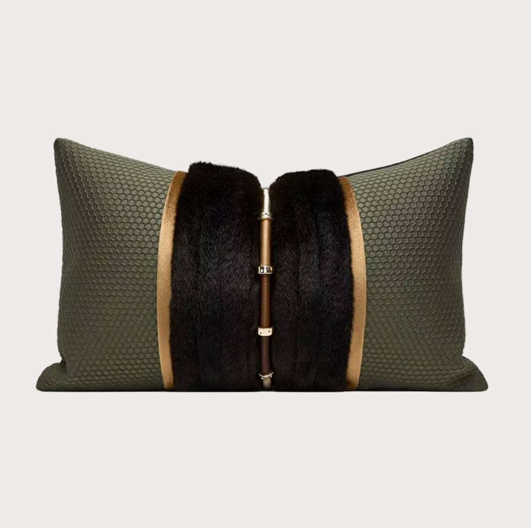 An olive green textured lumbar pillow featuring a central black fur panel and a vertical gold-tone metal rod with decorative rings.