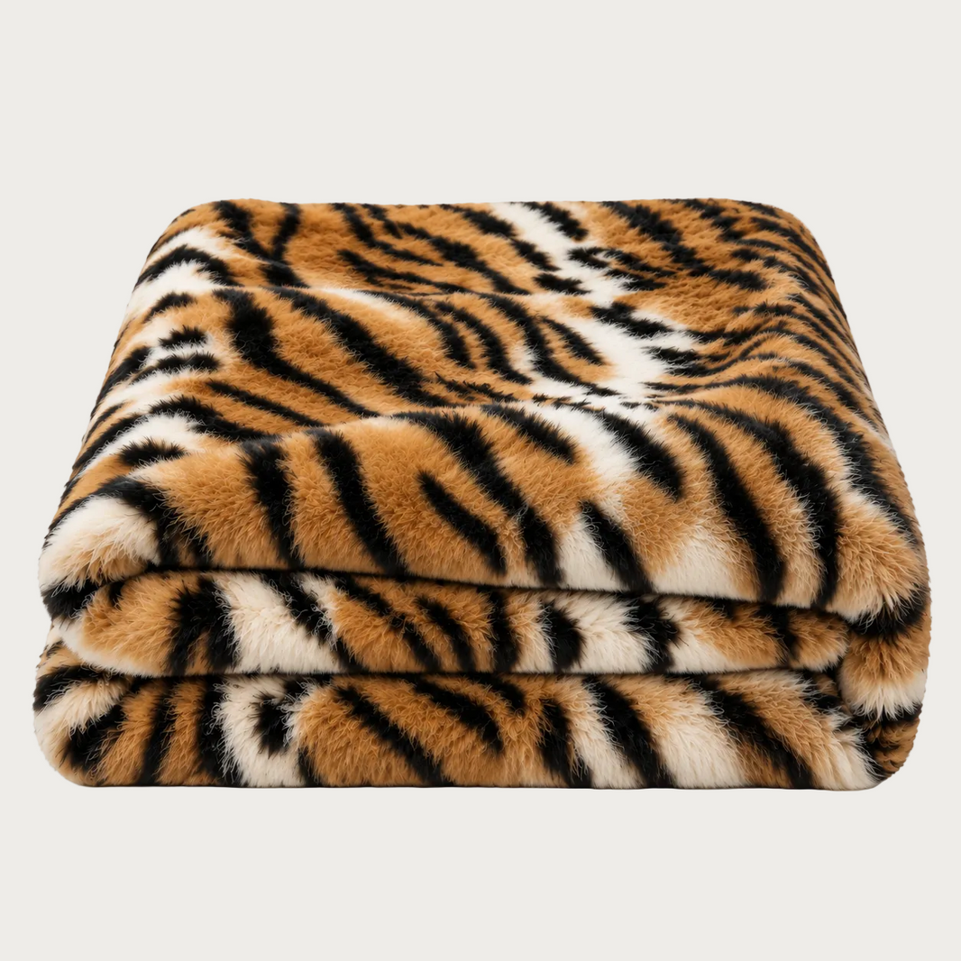A folded plush faux-fur blanket with a tiger stripe pattern in orange, black, and cream, shown on a clean white background.
